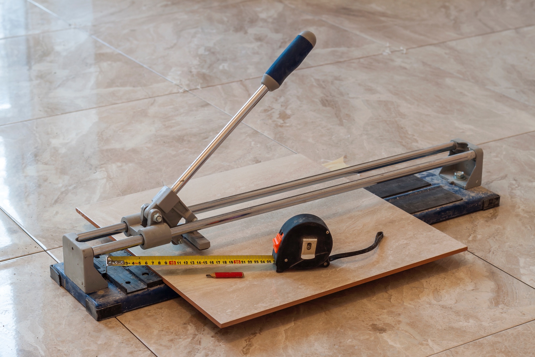 A tile cutting tool sits on a tile floor, cutting a new tile to size for installation.
