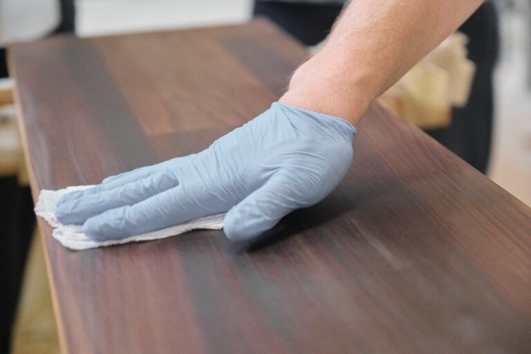 A worker’s hand as he polishes a piece of dark stained wood.