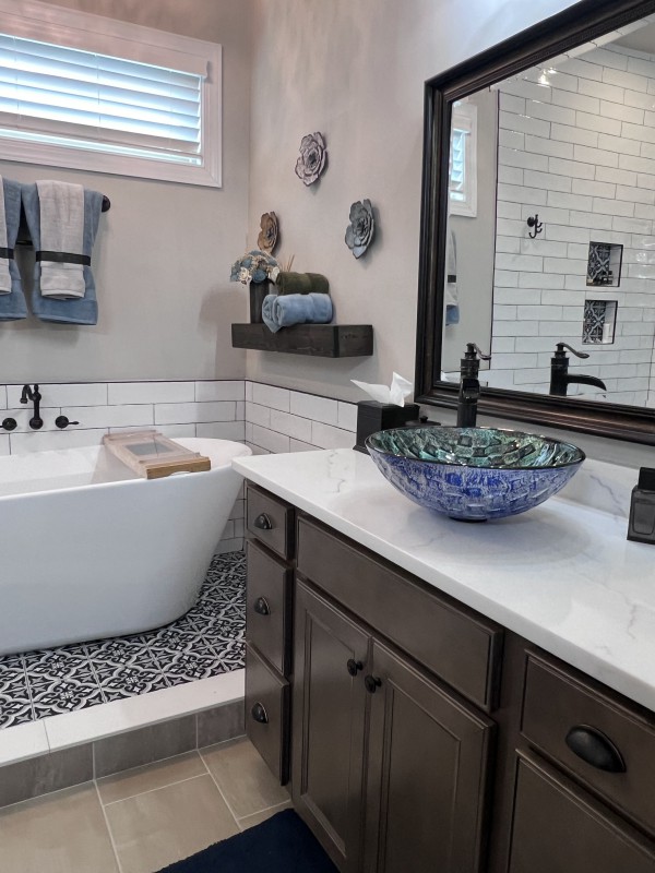 Luxurious bathroom interior with a freestanding tub, unique blue glass vessel sink on a granite countertop, and elegant decor enhancing the serene aesthetic as part of a complete bathroom renovation.